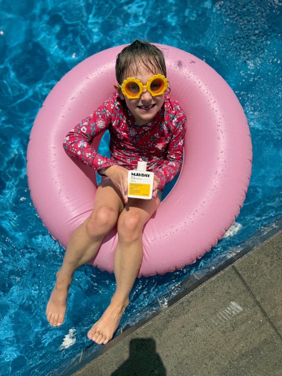 Child in a pool float wearing sunglasses and holding MAYDAY sunscreen